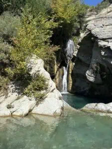 שלט רחוק של מפלי מים בטירה אלבניה עם טבע lush ירוק ומים כחולים בהירים.