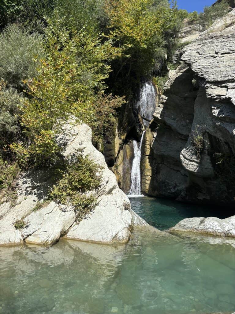 שלט רחוק של מפלי מים בטירה אלבניה עם טבע lush ירוק ומים כחולים בהירים.